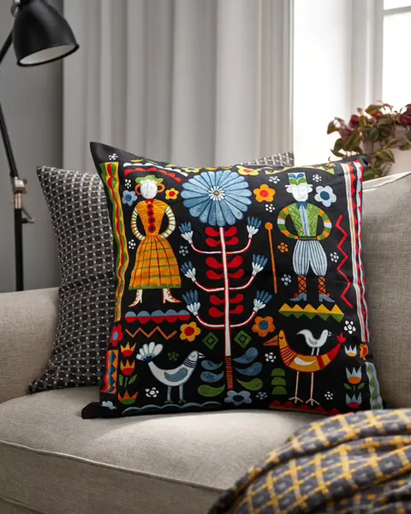 Embroidered black cushion cover and a patterned grey cushion on a pale grey sofa, with a yellow and grey throw over the arm